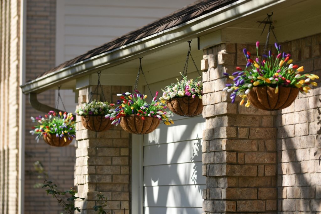 A sunny veranda features floral hanging baskets with colorful blooms under a brick roof.