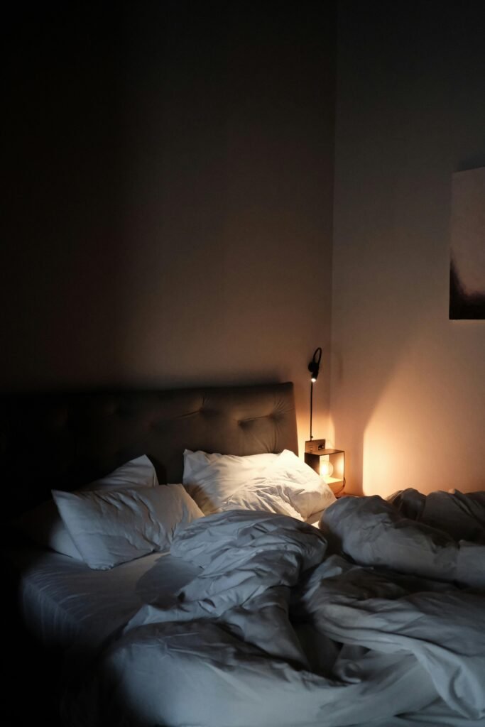 A warm, dimly lit bedroom featuring a neatly arranged bed with pillows and a soft glow from a bedside lamp.