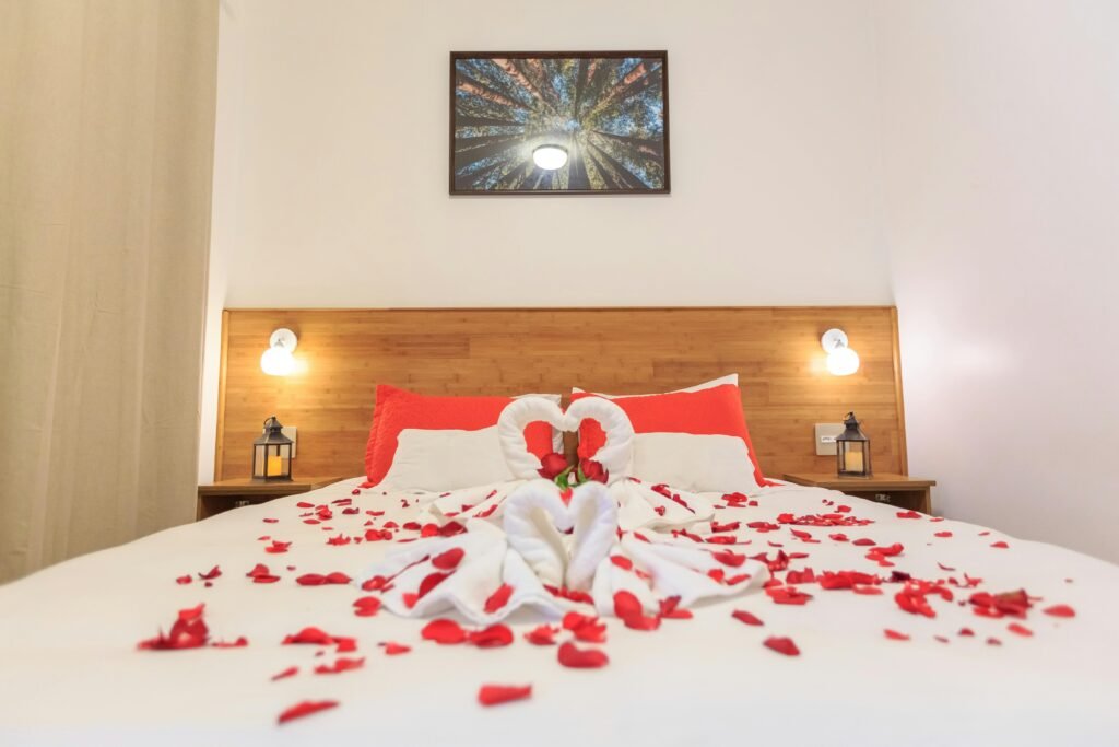 Cozy bedroom setup with red rose petals and towel swans for a romantic atmosphere.