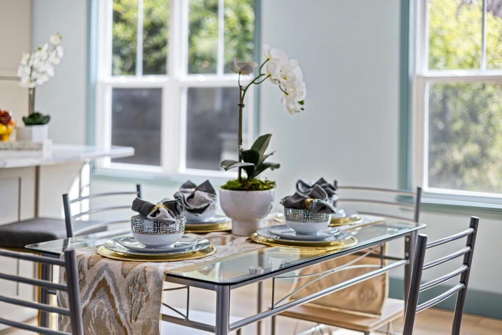 A beautifully set dining table with elegant decor and a glass tabletop, featuring minimalist and modern design elements.