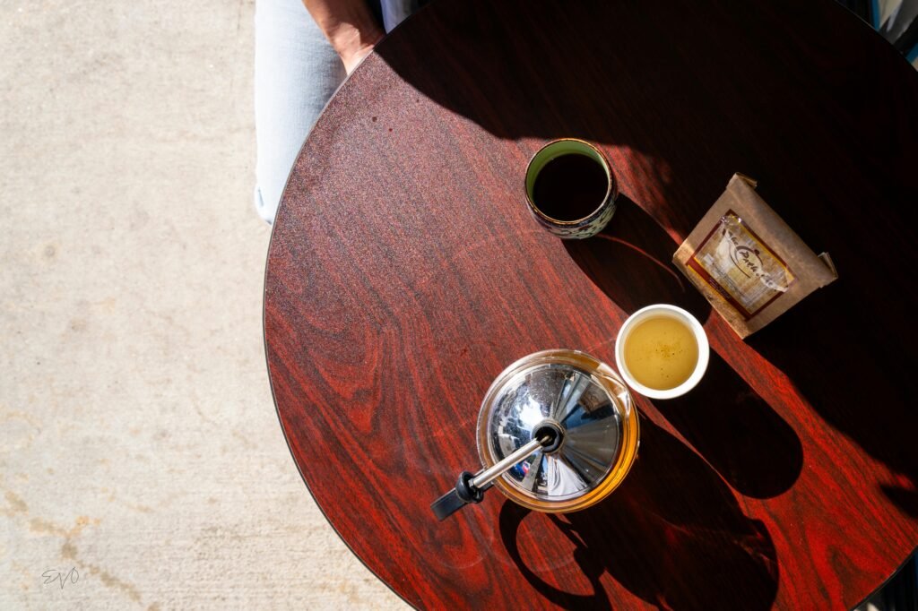 Top-down view of a wooden table with tea, a French press, and sunlight casting shadows.